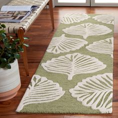 a green and white rug with leaves on it in front of a wooden bench next to a potted plant