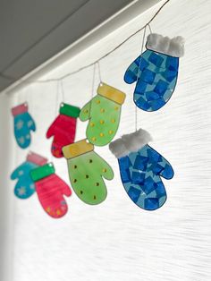 colorful handmade mitts hanging from a line on a window sill in the daytime