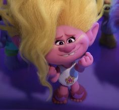 an animated troll with blonde hair standing in front of some other cartoon characters and looking at the camera