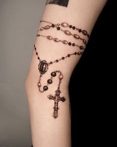 a woman's arm with a rosary and cross tattoo on the left side of her arm