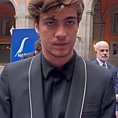 a man in a suit and tie standing next to another man wearing a black shirt