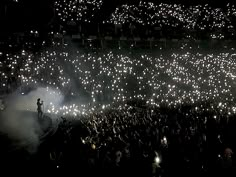 a large group of people standing on top of a field with fireworks in the air