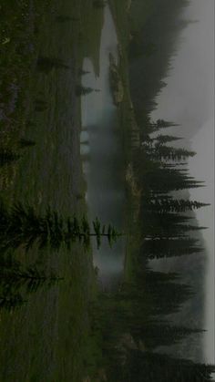 an animal is standing in the grass next to some water and trees with fog on them