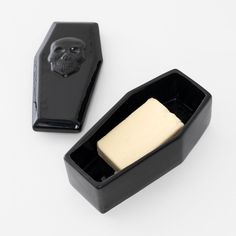 a skull shaped soap dish next to a black container with a bar of soap in it