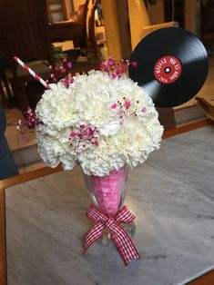 a vase filled with white and pink flowers sitting on top of a table next to a record