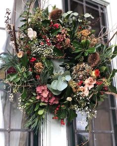 a wreath hanging on the side of a building with flowers and greenery around it