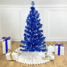 a blue christmas tree surrounded by presents on a wooden floor with white walls in the background