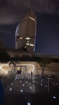 people are standing in front of a building at night with lights on the ground and around it