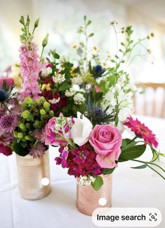 two vases filled with flowers sitting on top of a white tablecloth covered table