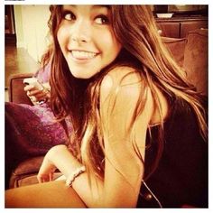 a young woman sitting on top of a couch next to a purple pillow and smiling at the camera