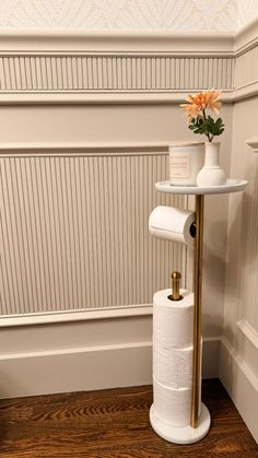 a toilet paper holder with two rolls of toilet paper on it and a flower in a vase