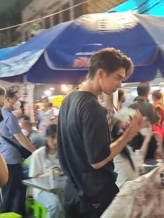 a man standing in front of a bunch of people at an outdoor food market looking at his cell phone