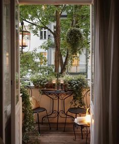 an open door leading to a balcony with potted plants on the table and two chairs