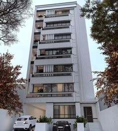 two cars parked in front of a tall white building with balconies on the second floor