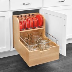 an open drawer in a kitchen filled with glasses and red plates on top of it