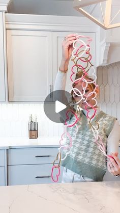 a woman standing in a kitchen next to a counter top holding up pink streamers