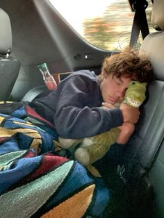 a young boy laying in the back seat of a car holding a stuffed animal and sleeping