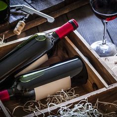 three wine bottles in a wooden box next to a glass of wine and corkscrews