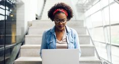 a woman in glasses using a laptop on the stairs with her headband around her neck