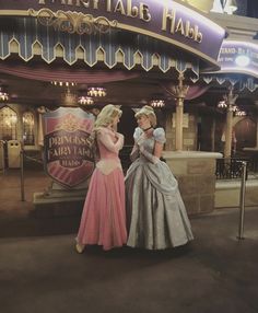 two women dressed as princesses standing in front of the entrance to an amusement park