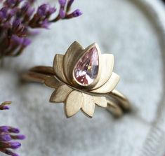 a gold ring with a pink stone in the center and purple flower petals around it