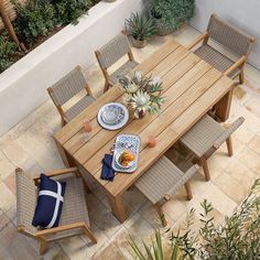 an outdoor dining table with chairs and plates on it, next to potted plants