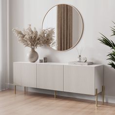 a white sideboard with a mirror on the wall and plants in vases next to it