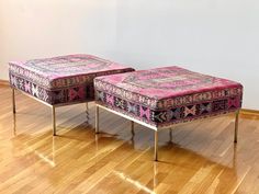 two pink ottomans sitting on top of a hard wood floor next to a white wall