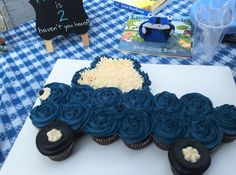 a table topped with blue frosted cupcakes next to a white cutting board