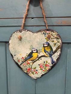 a heart shaped sign with two birds on it hanging from a rope against a blue door