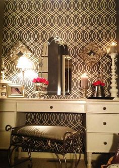 a dressing table with a mirror, stool and candle holders on it in front of an ornate wallpaper