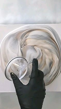 a person wearing black gloves and holding a glass in front of a white wall with swirls on it