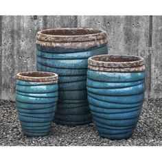 three large blue pots sitting next to each other on top of gravel covered ground in front of a concrete wall