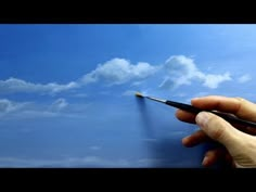 a person is holding a paintbrush in their left hand and painting the sky with clouds