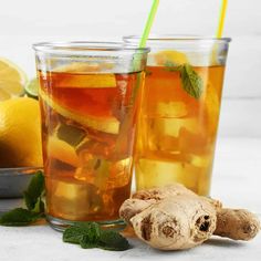 two glasses filled with iced tea next to sliced lemons and ginger on a table