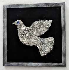 a silver bird with blue eyes in a black frame