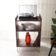 a record player sits on top of a shelf next to a red vase and books