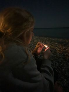 a woman sitting on the beach holding a lit candle in her hand and looking at the sky