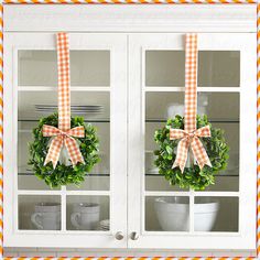 two wreaths are hanging on the glass front of a hutch with dishes and utensils