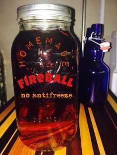 a glass jar filled with liquid sitting on top of a wooden table next to a blue bottle