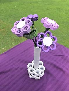 a vase filled with purple flowers on top of a purple table cloth covered field in the background