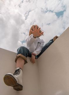 a young boy sitting on the edge of a wall with his hands up in the air