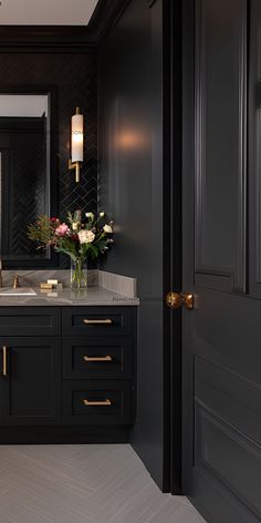 a bathroom with black cabinets and marble counter tops, along with flowers in a vase