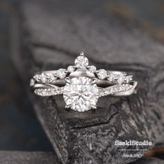 a white gold engagement ring with diamonds on top and side stones in the bottom, sitting on a rock