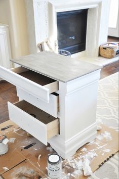 a white table with drawers and paint on the floor in front of a fire place