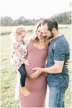 a man and woman holding a baby girl while standing in a field