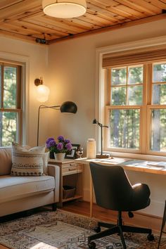 a living room with a couch, chair and desk in front of two large windows