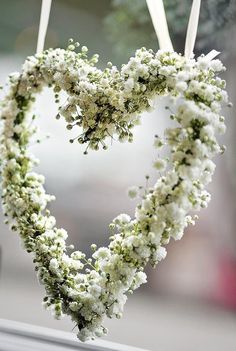 a heart shaped wreath with white flowers hanging from it's sides on a window sill