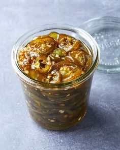 a glass jar filled with pickles on top of a gray table next to a bowl of food