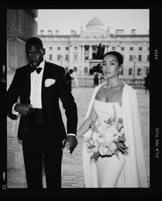 a black and white photo of a bride and groom in front of a large building